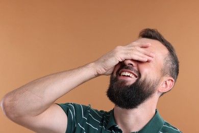 Photo of Man covering eyes and laughing on brown background
