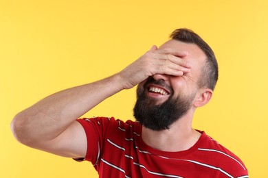 Photo of Man covering eyes and laughing on yellow background