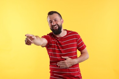 Photo of Handsome man pointing at something and laughing on yellow background