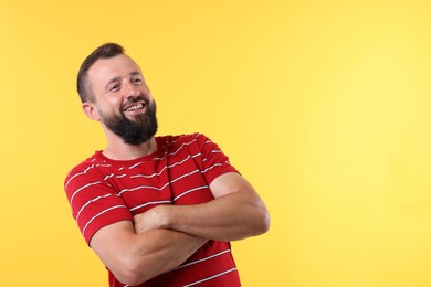 Photo of Handsome man with crossed arms laughing on yellow background. Space for text