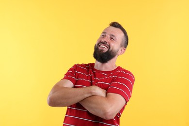 Photo of Handsome man with crossed arms laughing on yellow background