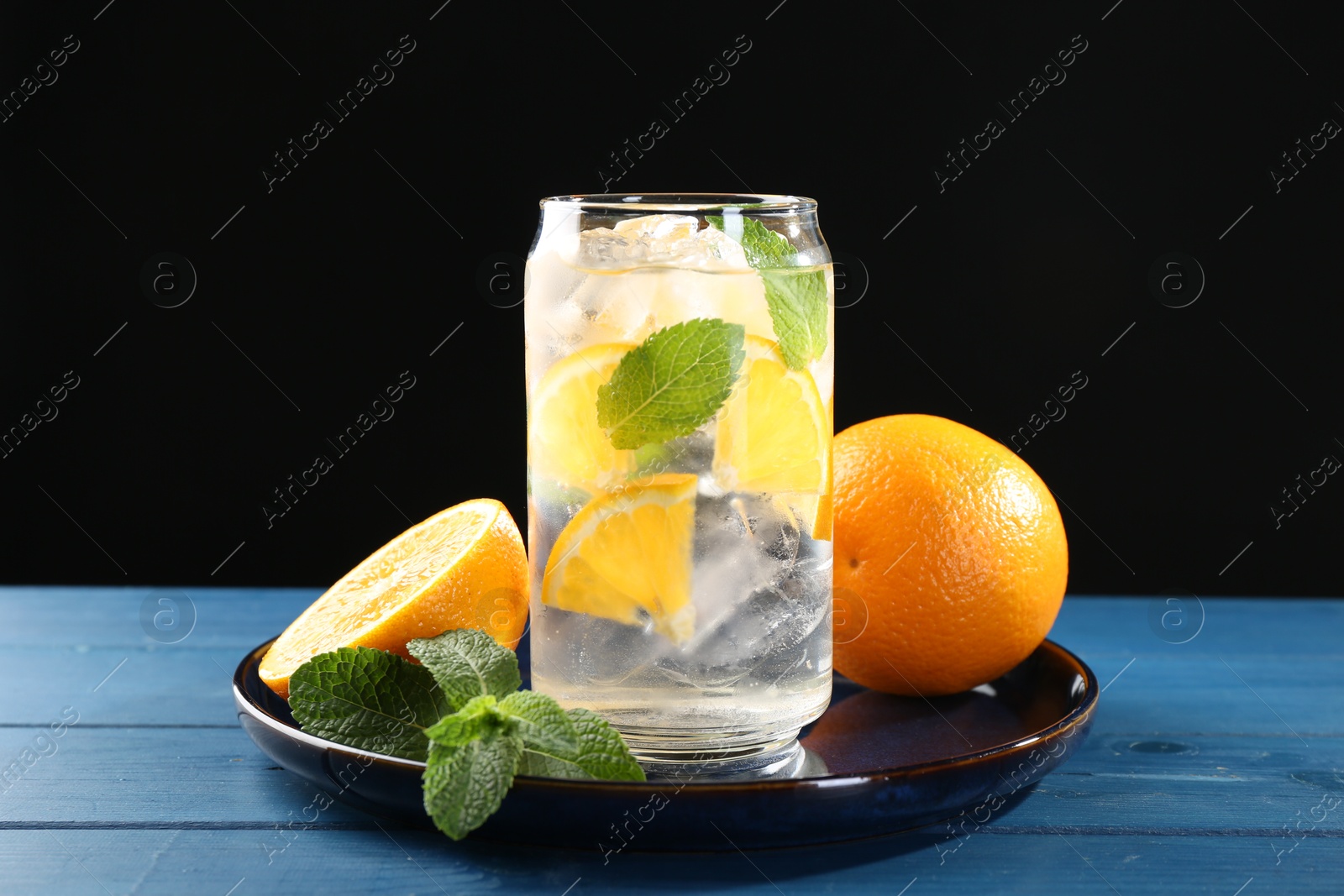 Photo of Sparkling water with orange, ice and mint in glass on blue wooden table, closeup