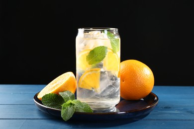 Photo of Sparkling water with orange, ice and mint in glass on blue wooden table, closeup