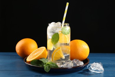 Photo of Sparkling water with orange, ice and mint in glass on blue wooden table, closeup