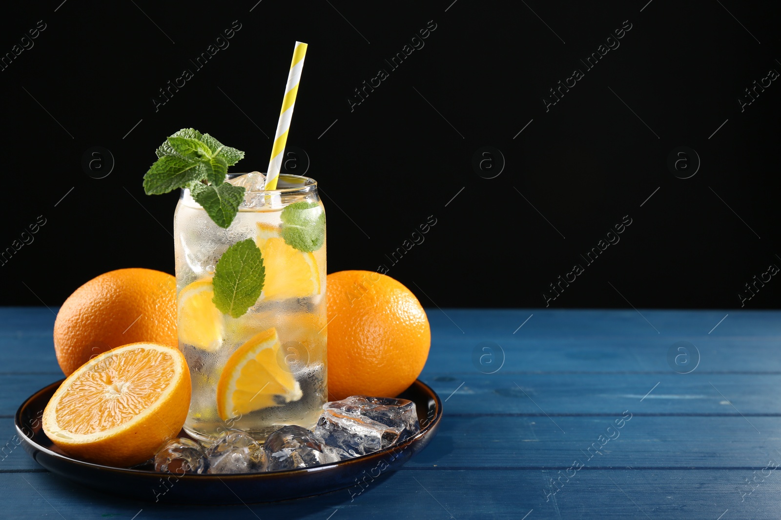 Photo of Sparkling water with orange, ice and mint in glass on blue wooden table, closeup. Space for text