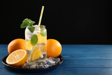 Photo of Sparkling water with orange, ice and mint in glass on blue wooden table, closeup. Space for text