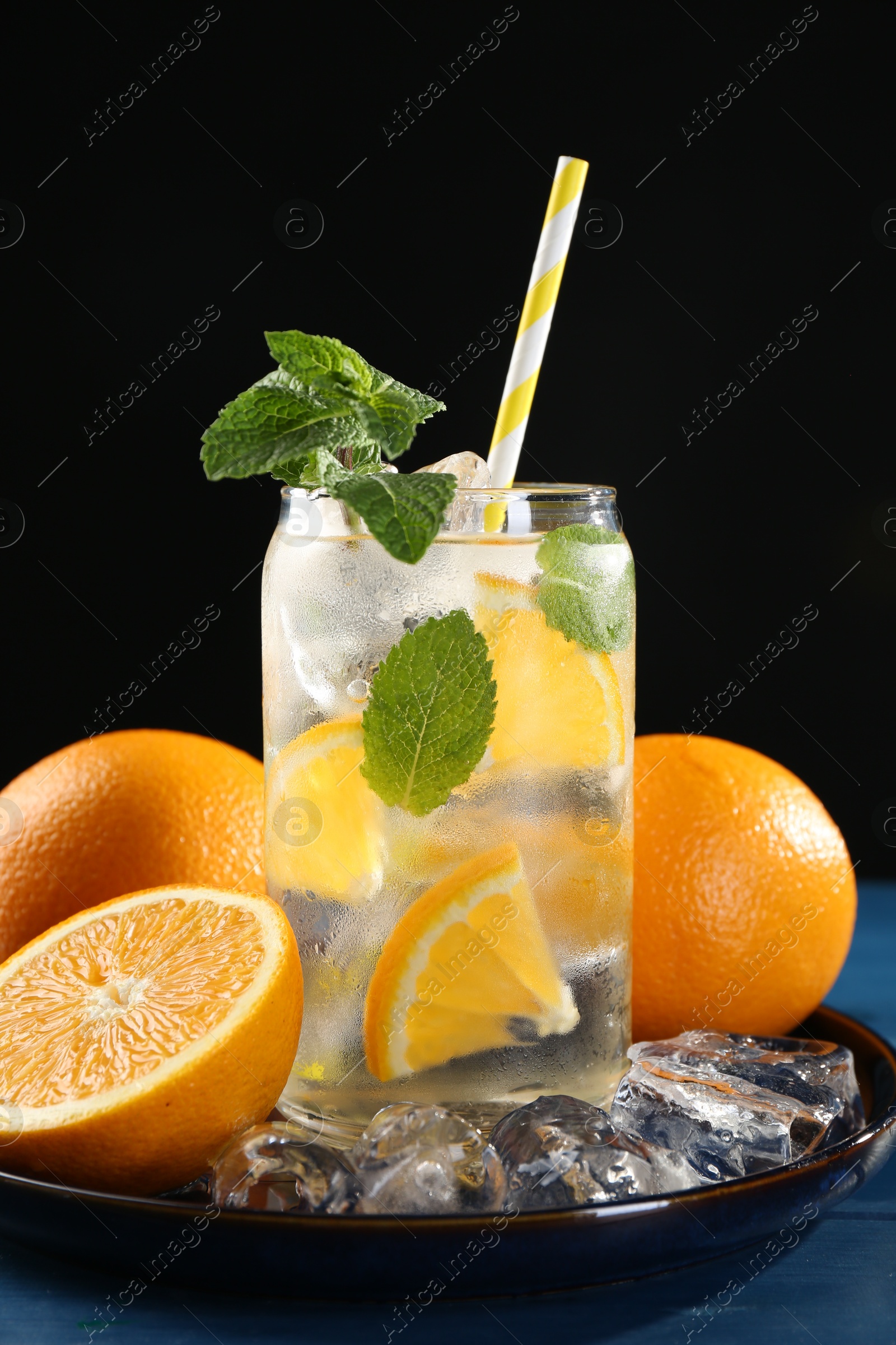 Photo of Sparkling water with orange, ice and mint in glass on blue wooden table, closeup