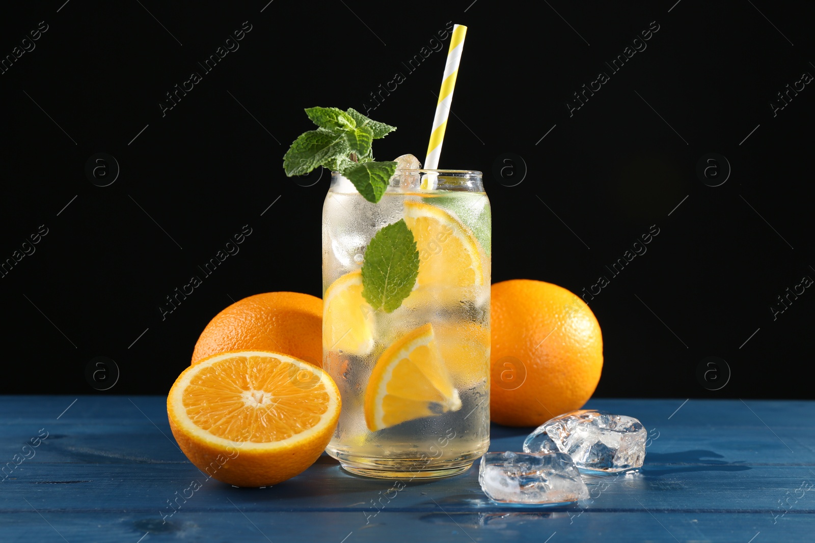 Photo of Sparkling water with orange, ice and mint in glass on blue wooden table, closeup