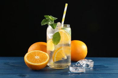 Photo of Sparkling water with orange, ice and mint in glass on blue wooden table, closeup