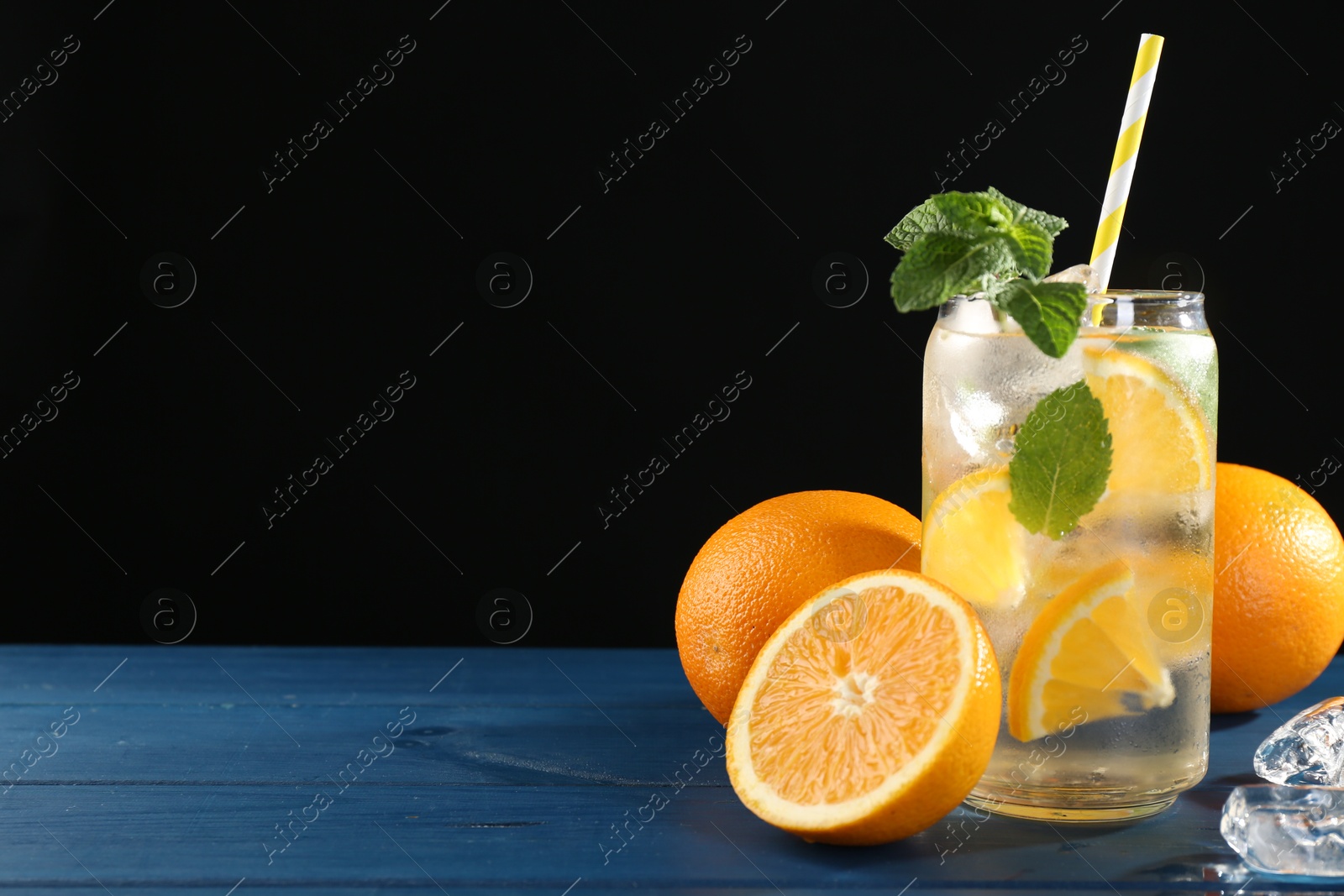 Photo of Sparkling water with orange, ice and mint in glass on blue wooden table, closeup. Space for text