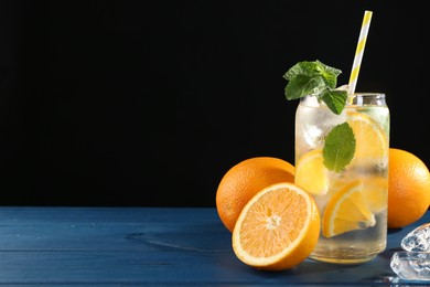 Photo of Sparkling water with orange, ice and mint in glass on blue wooden table, closeup. Space for text