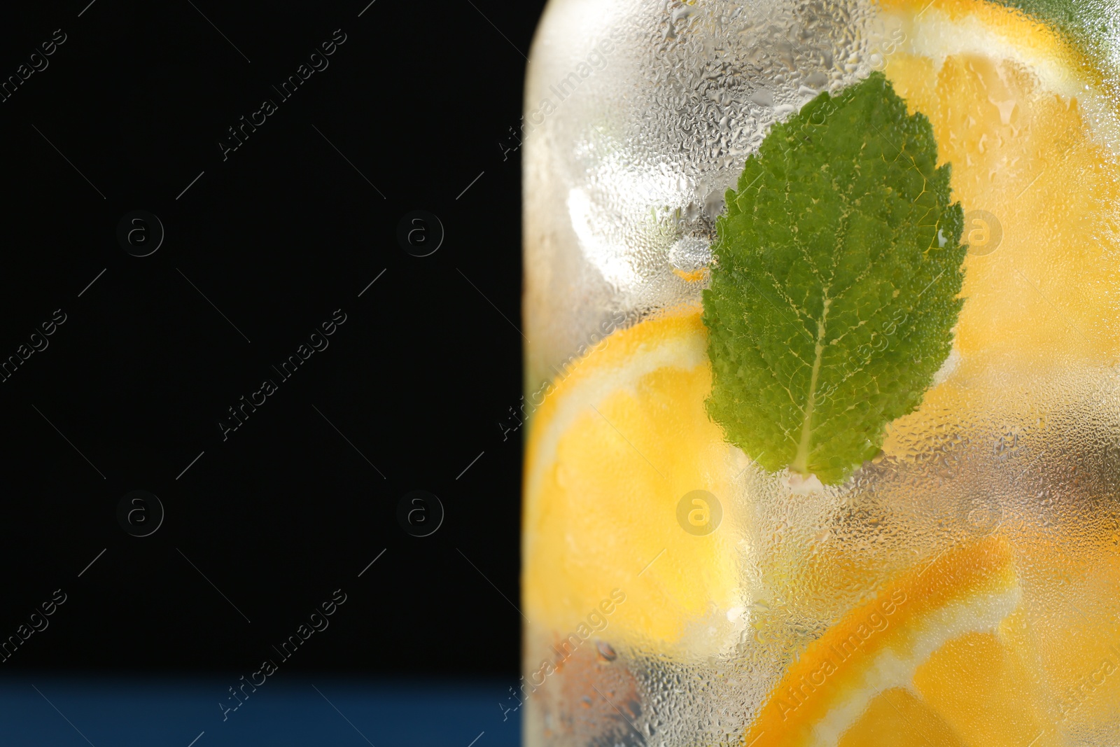 Photo of Sparkling water with orange and mint in glass on black background, closeup. Space for text