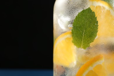 Photo of Sparkling water with orange and mint in glass on black background, closeup. Space for text