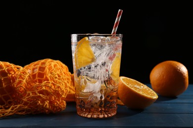 Photo of Sparkling water with orange in glass and fresh fruits on blue wooden table, closeup