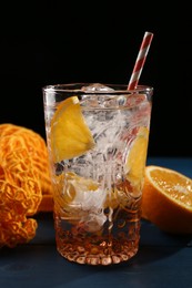 Photo of Sparkling water with orange in glass and fresh fruits on blue wooden table, closeup