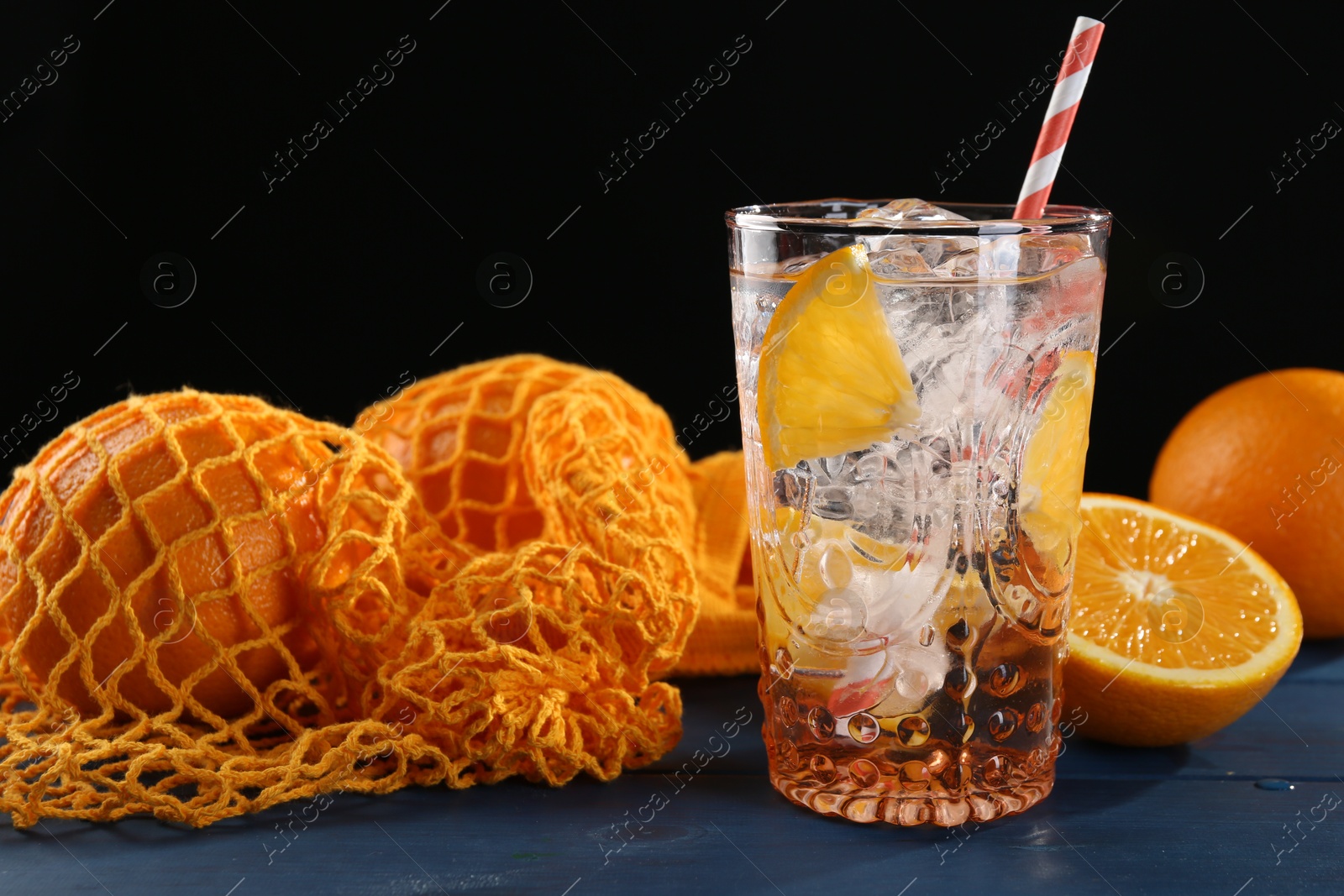 Photo of Sparkling water with orange in glass and fresh fruits on blue wooden table, closeup