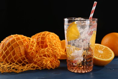 Photo of Sparkling water with orange in glass and fresh fruits on blue wooden table, closeup