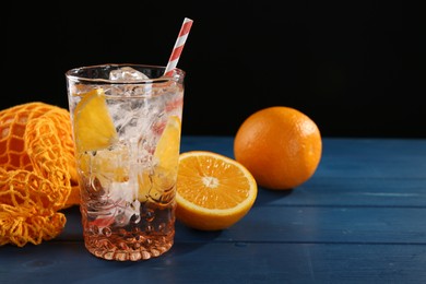 Photo of Sparkling water with orange in glass and fresh fruits on blue wooden table, closeup. Space for text