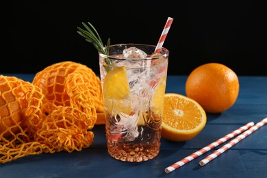 Photo of Sparkling water with orange in glass, fresh fruits and straws on blue wooden table, closeup