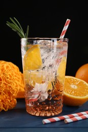 Photo of Sparkling water with orange in glass, fresh fruits and straws on blue wooden table, closeup