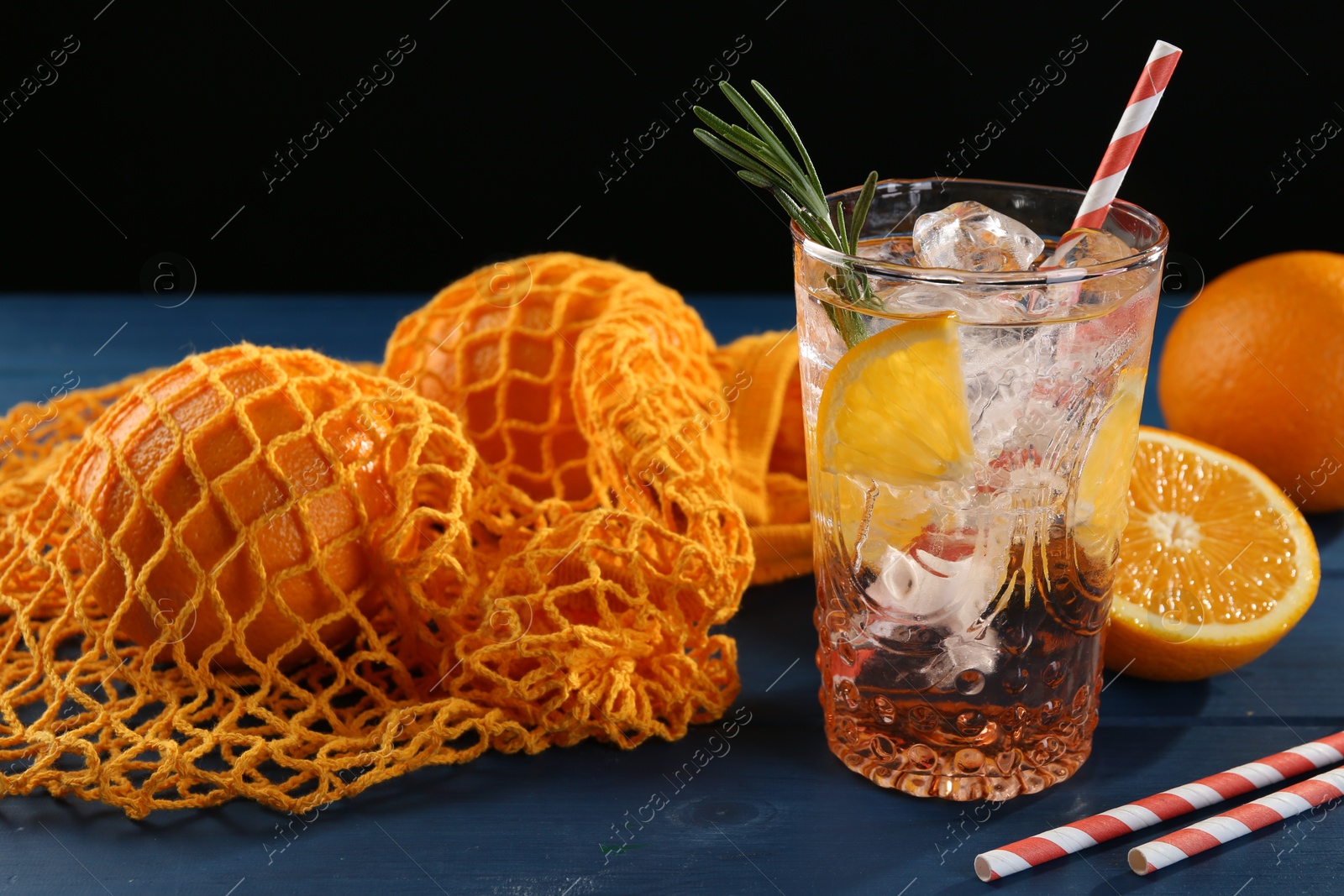 Photo of Sparkling water with orange in glass, fresh fruits and straws on blue wooden table, closeup