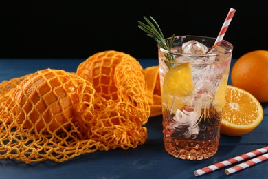 Photo of Sparkling water with orange in glass, fresh fruits and straws on blue wooden table, closeup