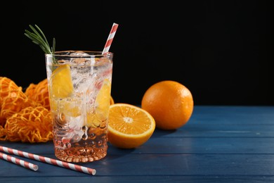 Photo of Sparkling water with orange in glass, fresh fruits and straws on blue wooden table, closeup. Space for text