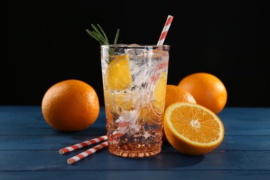 Photo of Sparkling water with orange in glass, fresh fruits and straws on blue wooden table, closeup