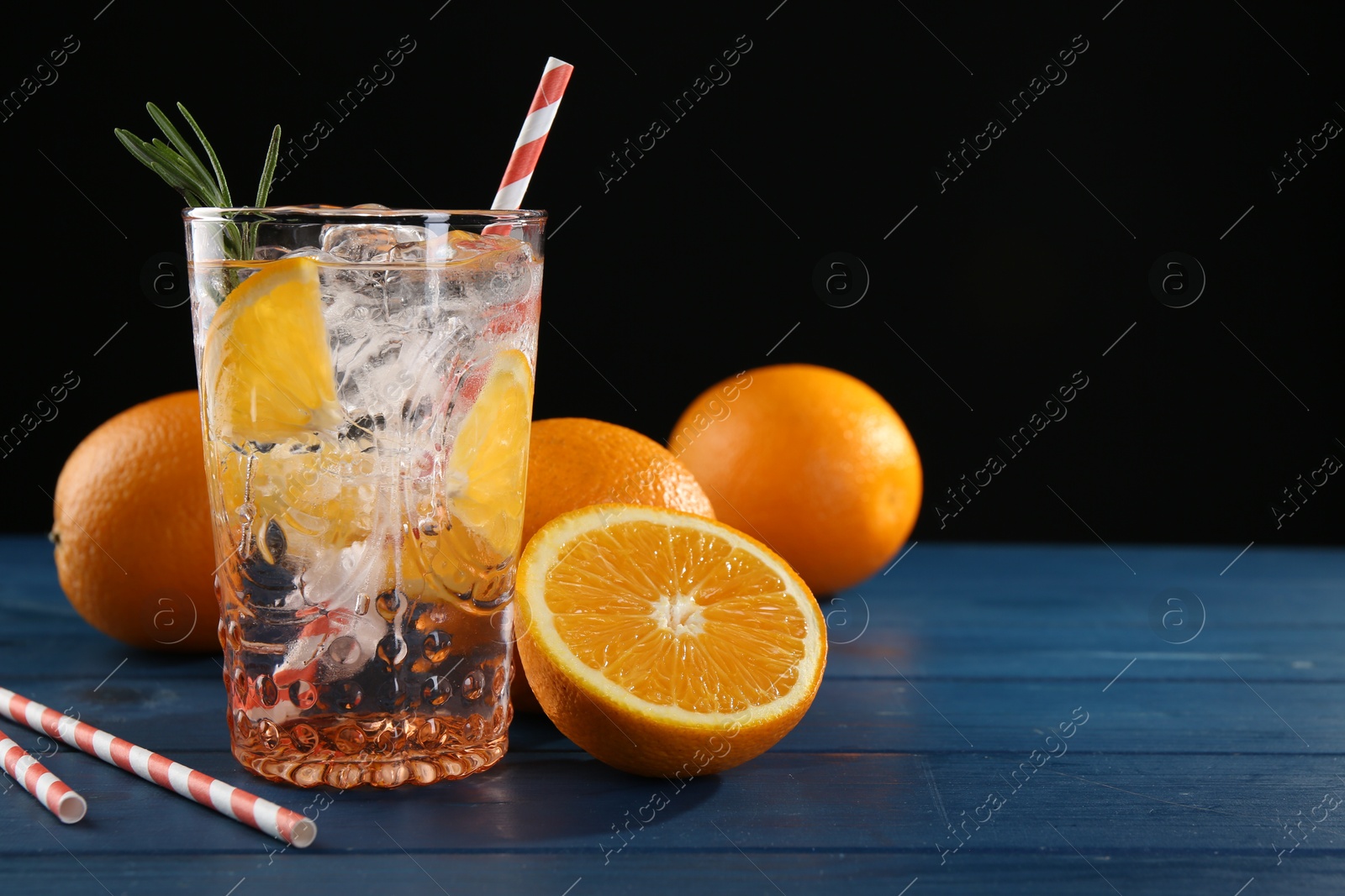 Photo of Sparkling water with orange in glass, fresh fruits and straws on blue wooden table, closeup. Space for text