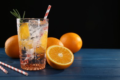Photo of Sparkling water with orange in glass, fresh fruits and straws on blue wooden table, closeup. Space for text