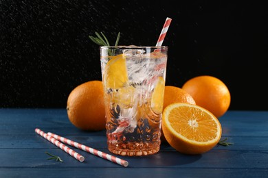 Photo of Sparkling water with orange in glass, fresh fruits and straws on blue wooden table, closeup