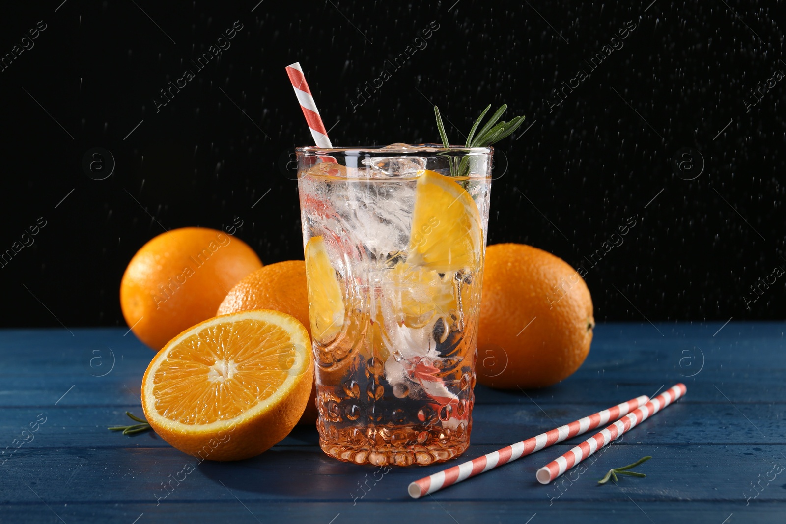 Photo of Sparkling water with orange in glass, fresh fruits and straws on blue wooden table, closeup