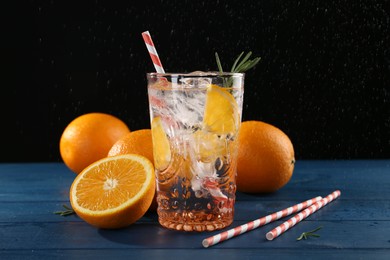 Photo of Sparkling water with orange in glass, fresh fruits and straws on blue wooden table, closeup