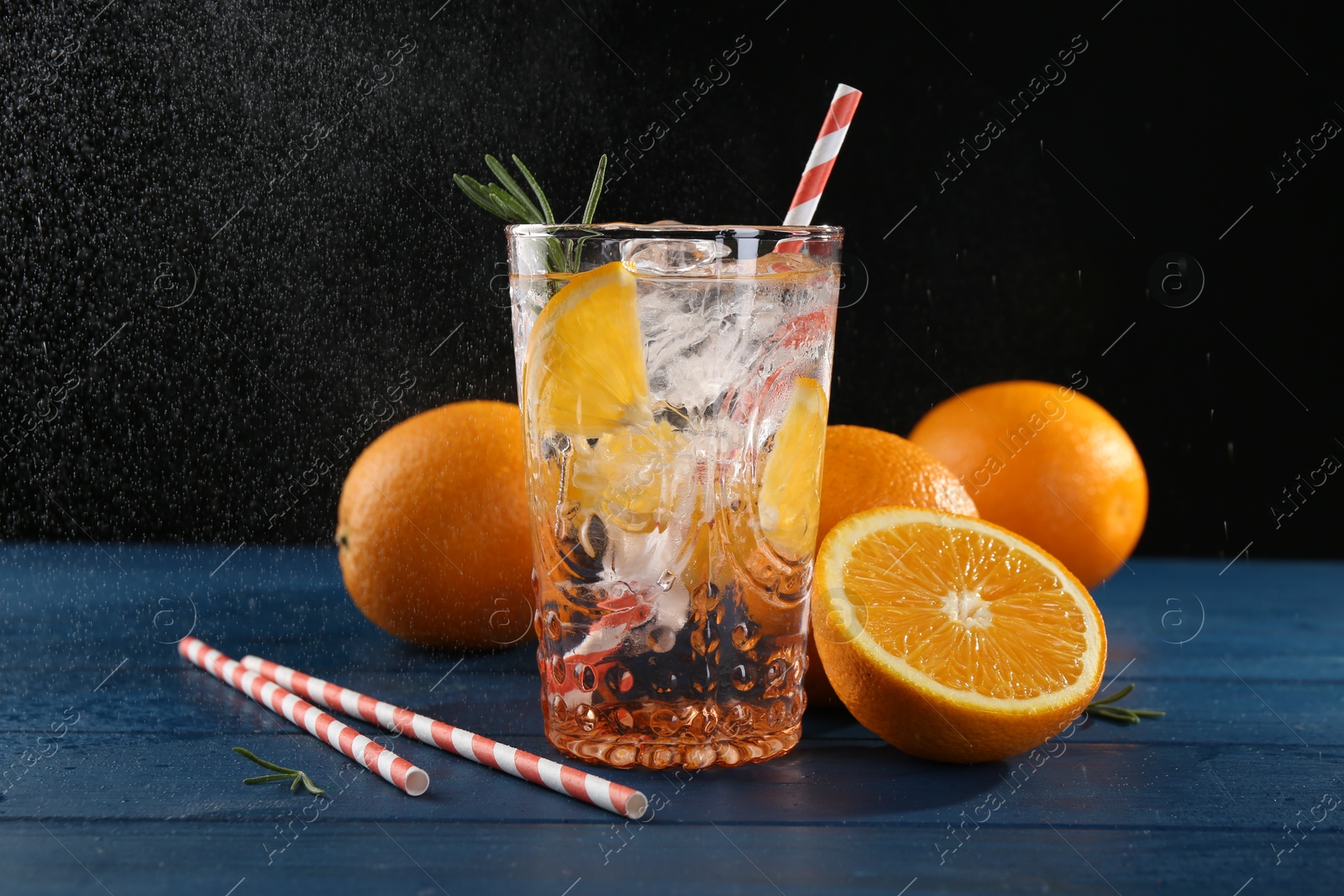 Photo of Sparkling water with orange in glass, fresh fruits and straws on blue wooden table, closeup
