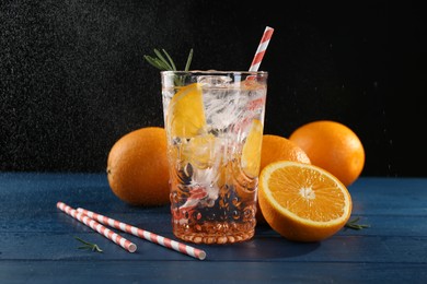 Photo of Sparkling water with orange in glass, fresh fruits and straws on blue wooden table, closeup