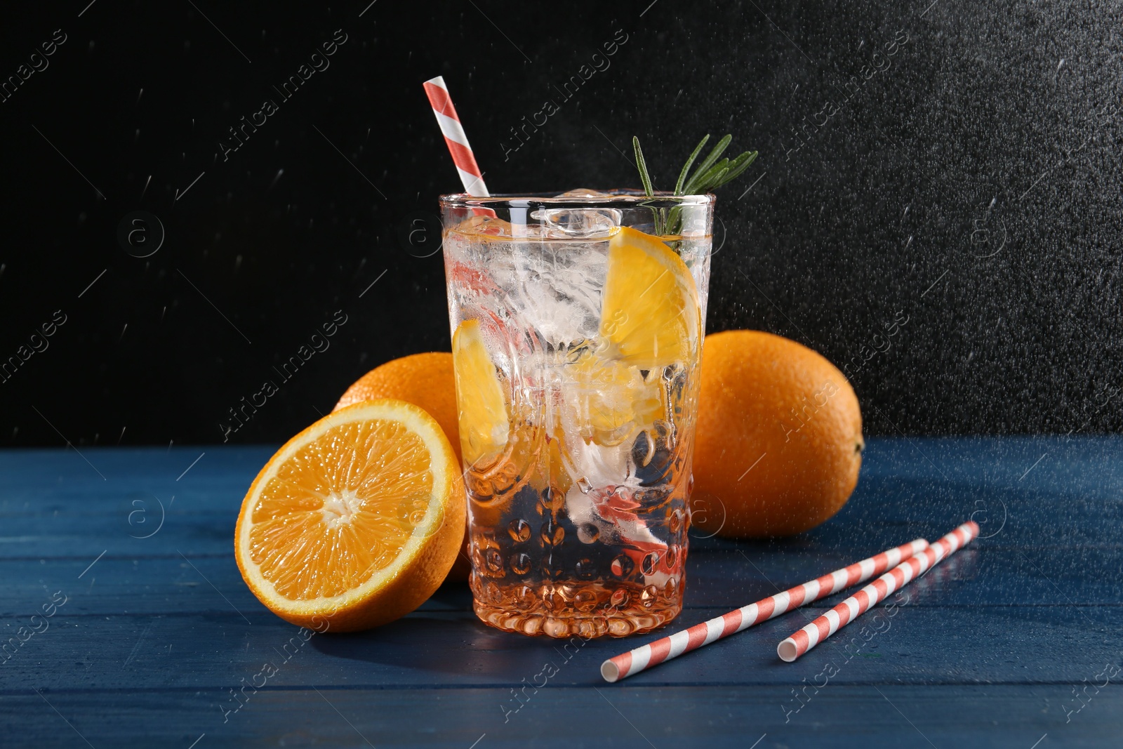 Photo of Sparkling water with orange in glass, fresh fruits and straws on blue wooden table, closeup