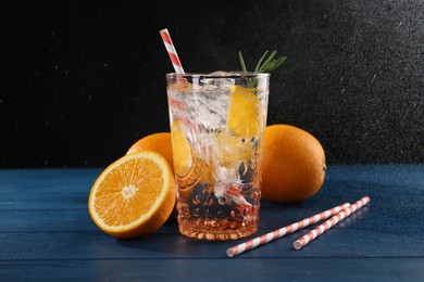 Photo of Sparkling water with orange in glass, fresh fruits and straws on blue wooden table, closeup