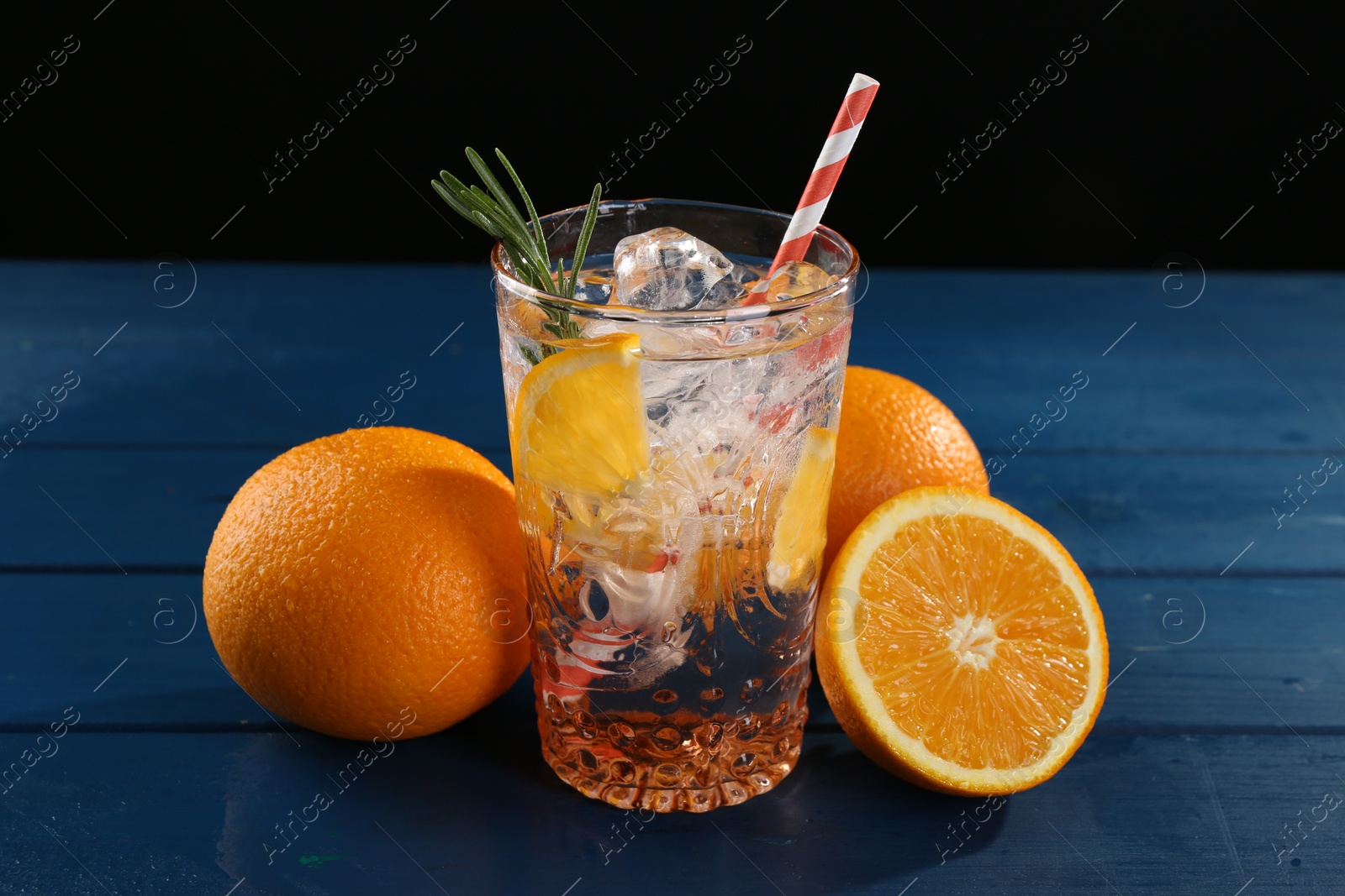 Photo of Sparkling water with orange in glass and fresh fruits on blue wooden table, closeup