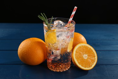 Photo of Sparkling water with orange in glass and fresh fruits on blue wooden table, closeup