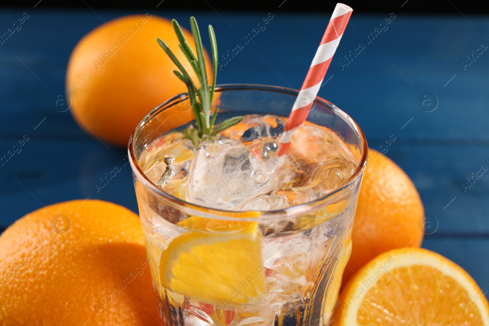Photo of Refreshing soda water with ice and orange on blue table, closeup
