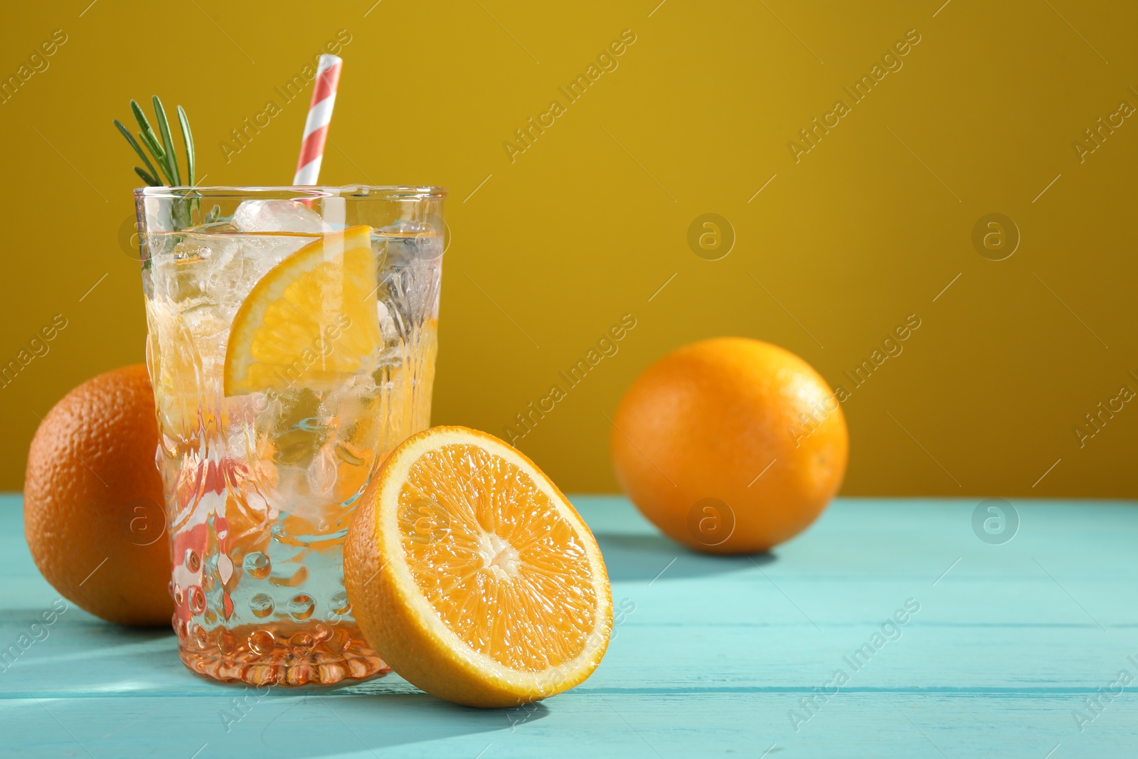 Photo of Refreshing soda water with ice and orange on light blue wooden table, closeup. Space for text