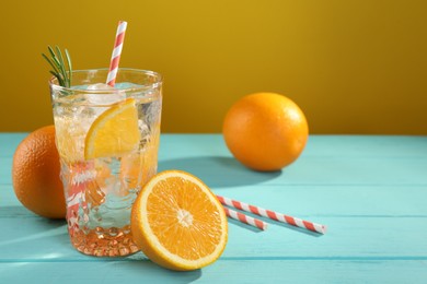 Photo of Refreshing soda water with ice and orange on light blue wooden table, closeup. Space for text