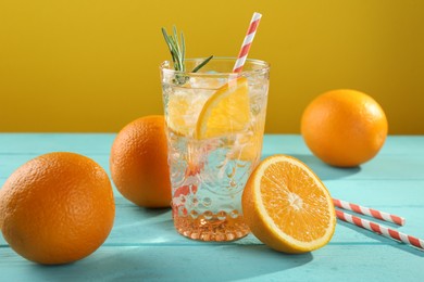 Photo of Refreshing soda water with ice and orange on light blue wooden table, closeup