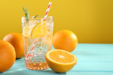 Photo of Refreshing soda water with ice and orange on light blue wooden table, closeup. Space for text