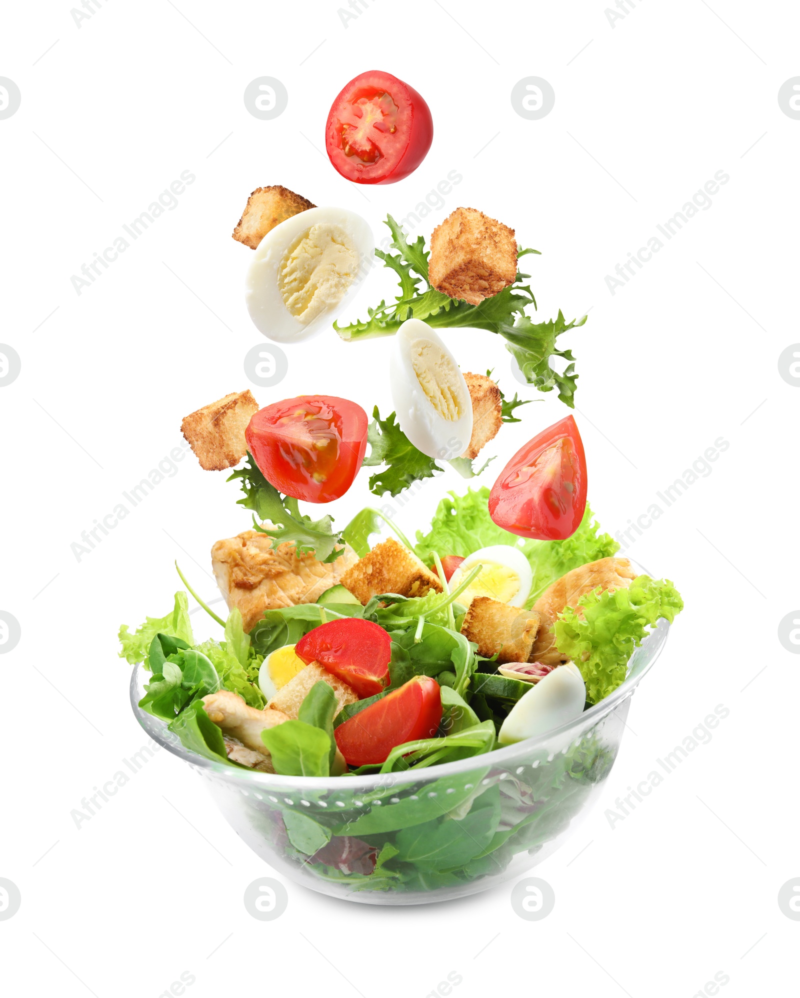 Image of Croutons and other ingredients falling into bowl of salad against white background