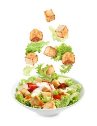 Image of Croutons and lettuce leaves falling into bowl of salad against white background