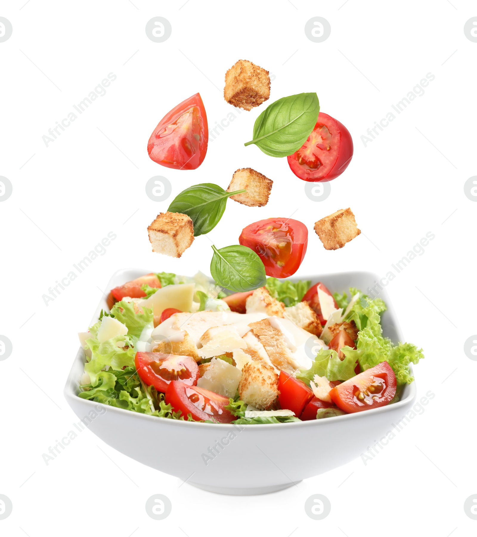 Image of Croutons and other ingredients falling into bowl of salad against white background