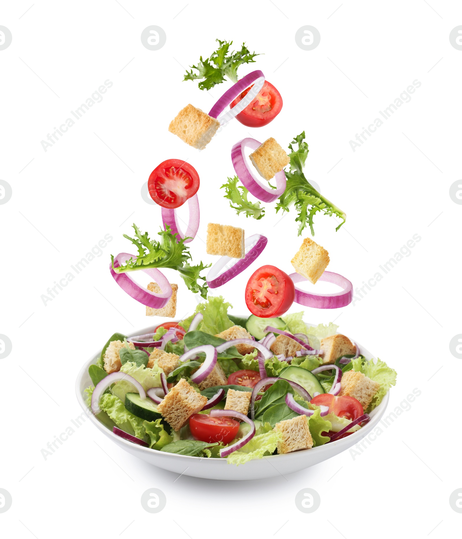 Image of Croutons and other ingredients falling into bowl of salad against white background