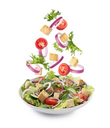 Image of Croutons and other ingredients falling into bowl of salad against white background
