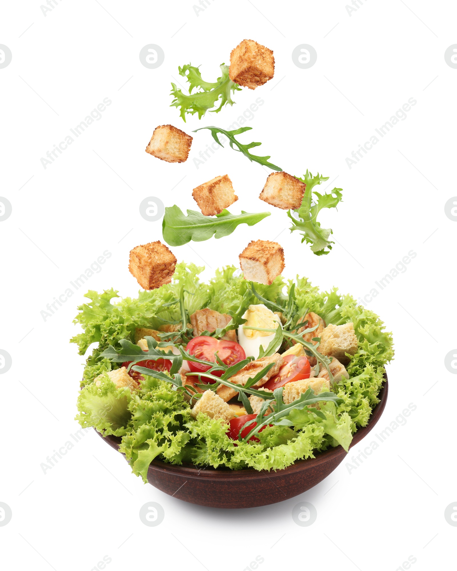 Image of Croutons and other ingredients falling into bowl of salad against white background